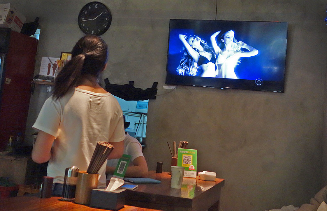 At a Beijing noodle joint, a wait staffer checks out a Victoria;s Secret fashion show on the wall TV.