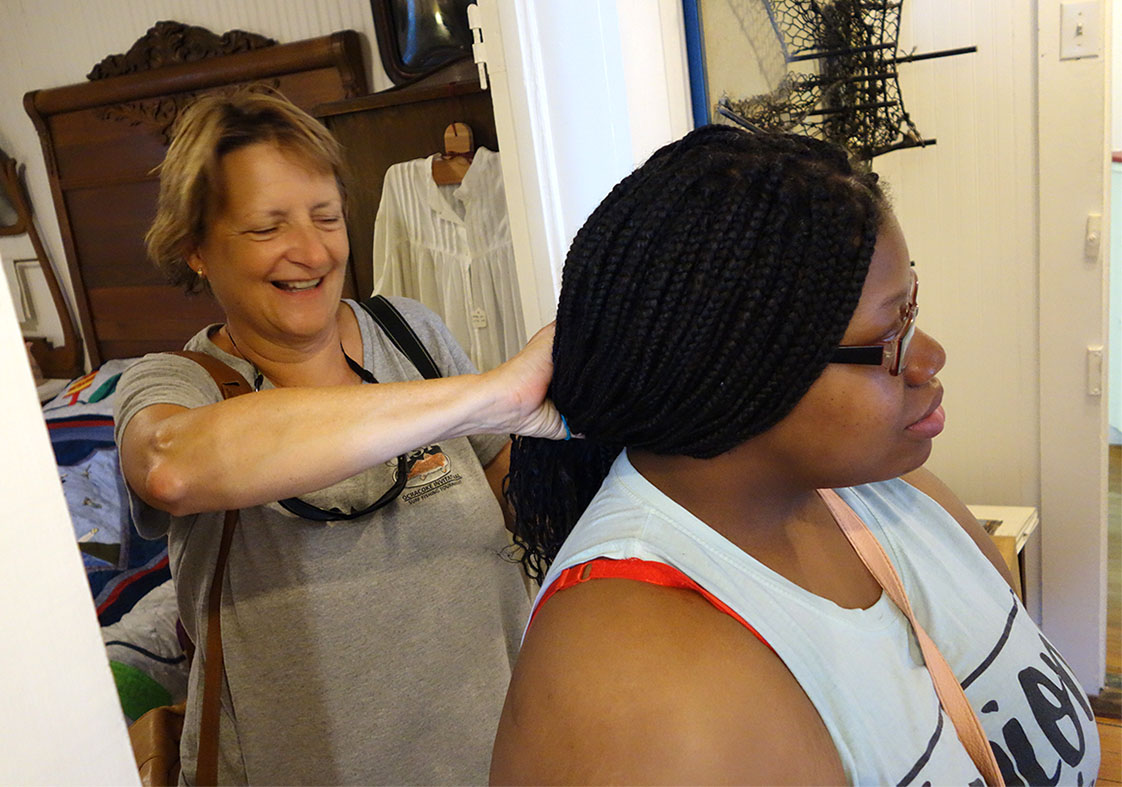 Getting to know you: Ocracoke Observer co-owner Connie Lienbach lends a hand, tying back PYO intern Christian Lawrence's braids during a tour of historic Ocracoke. (Jock Lauterer photo)