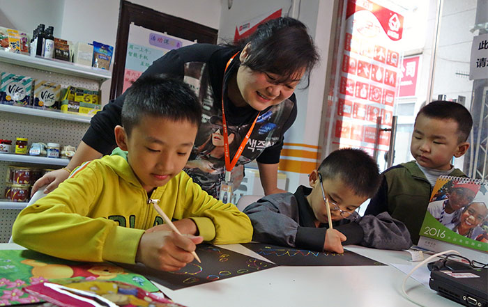 At the Glory City Station in Beijing, China, Station Director Zhao Na encourages young boys with their artwork. (Jock Lauterer photo)