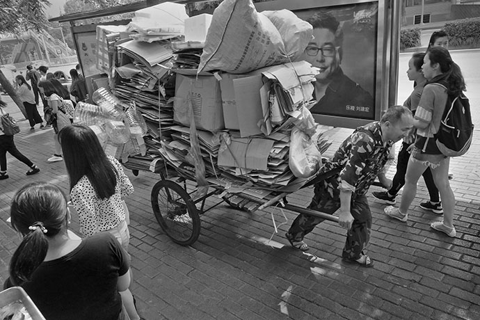 College kids, the hope of new China, stream by the sidewalk on the main drag across from campus in Chongqing as the local junkman hauls his immense load up the hill.