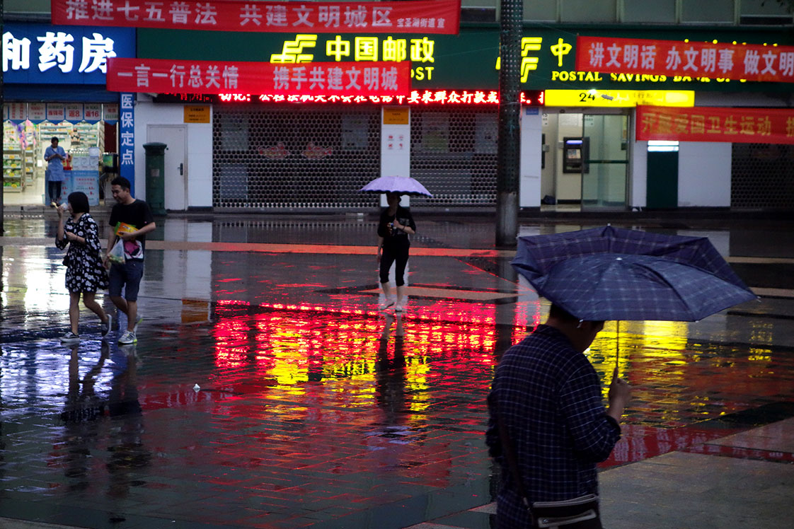 On a rainy night in old Chongqing, townspeople cross color-splashed square.